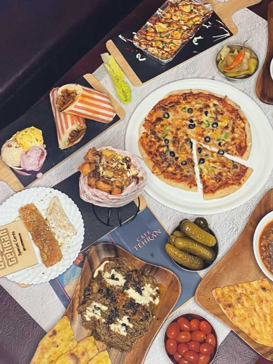 A flat lay of various Iranian dishes, including pizza, kebabs, and wraps.